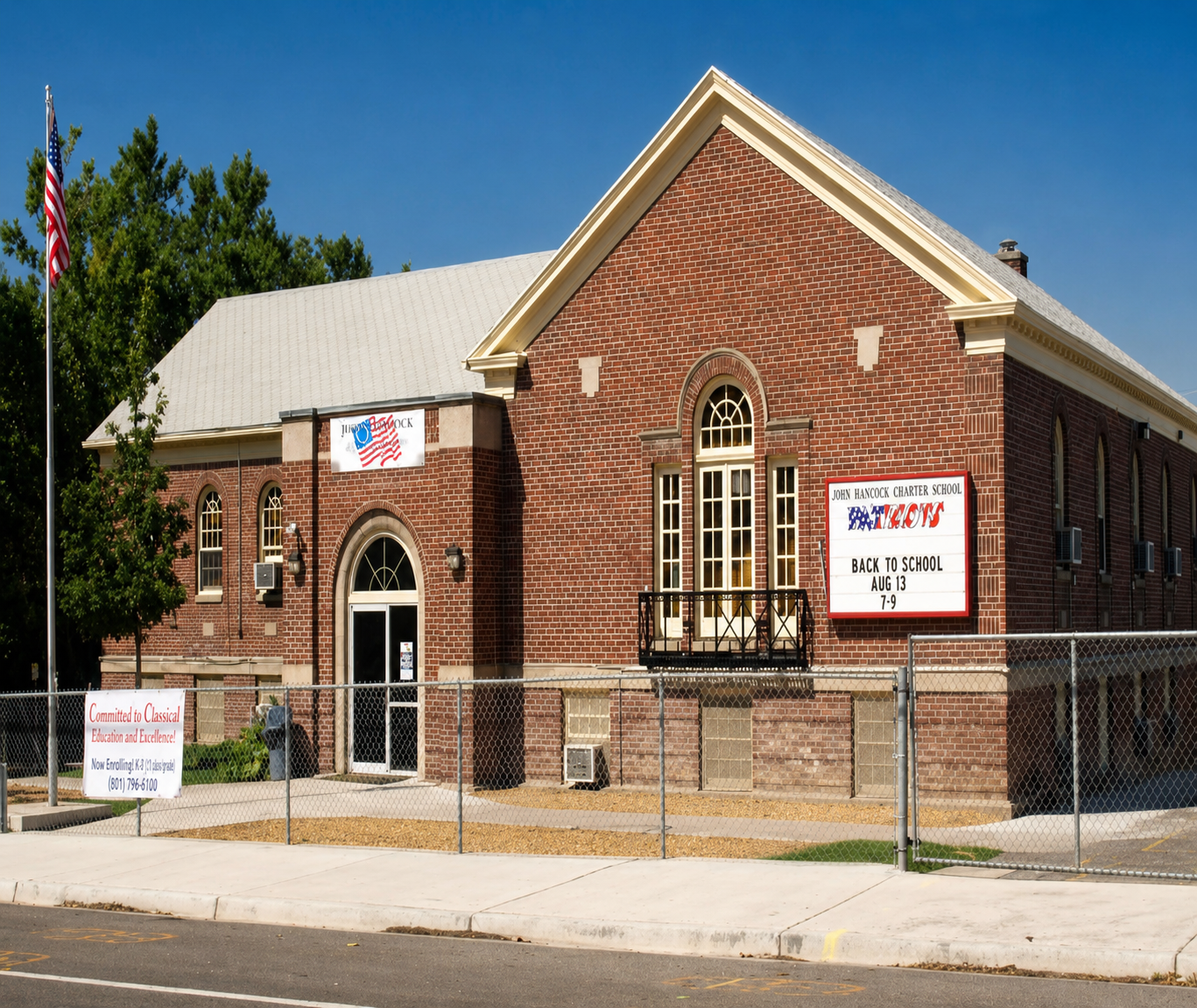 A single-story brick building with a gabled roof, arched windows, and an American flag flying outside.